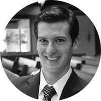 A black and white photo of Michael Thaney, who is smiling at the camera and wearing a suit and tie. 