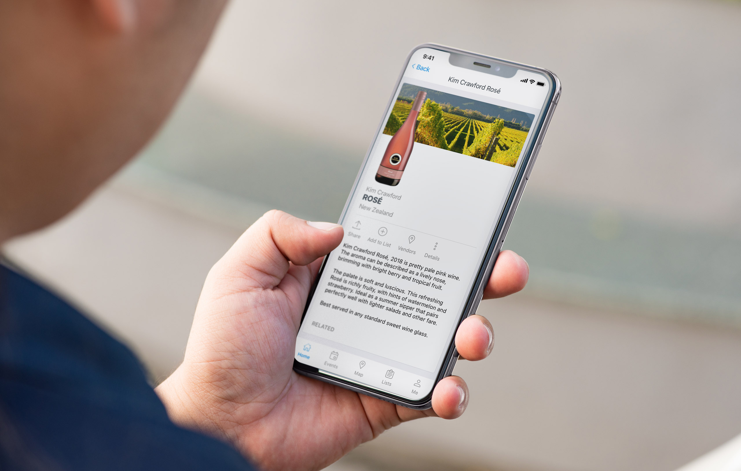 A man is holding an iPhone 11 in his left hand and he has the Ambassador app pulled up, which is displaying information about Kim Crawford rose wine.