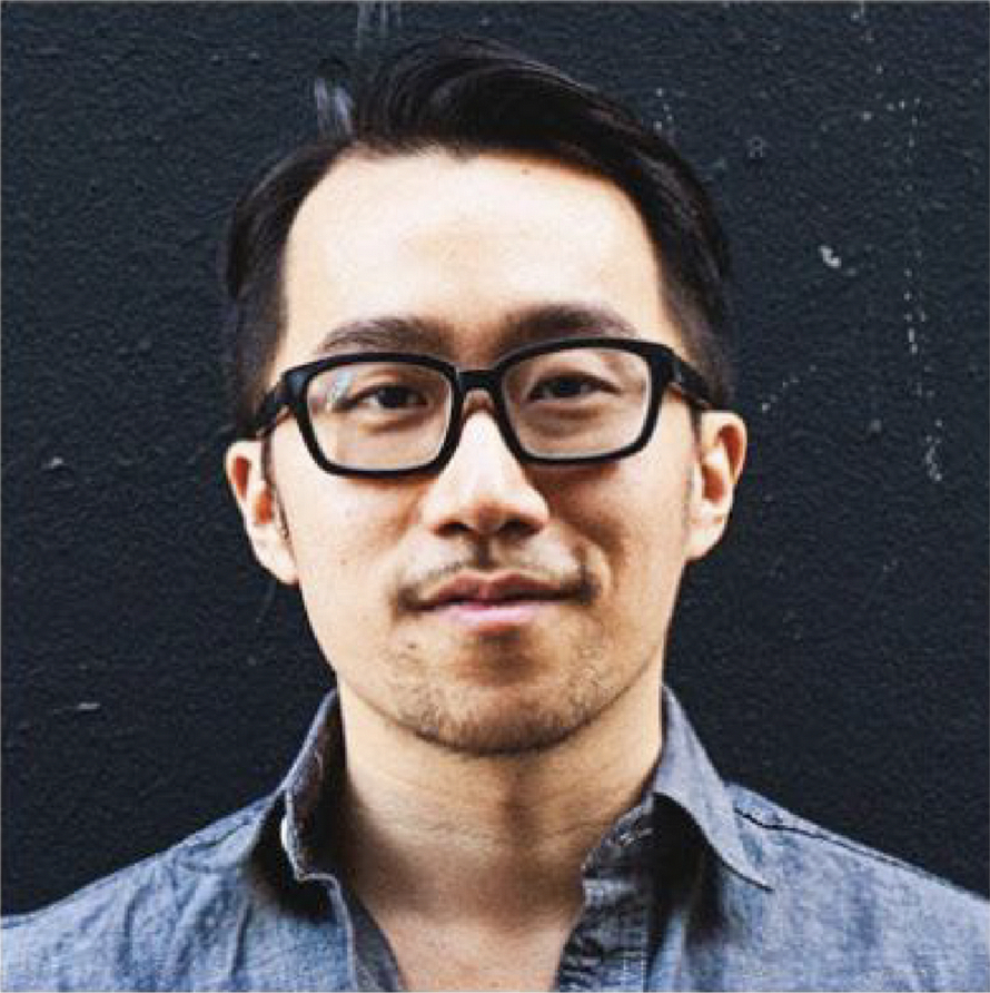 A portrait of the second user persona, Nate Young, who is an Asian man in his 30's – 40's. He's slightly smiling, has short dark hair, and is wearing matte black thick-framed glasses and a denim button-up shirt.